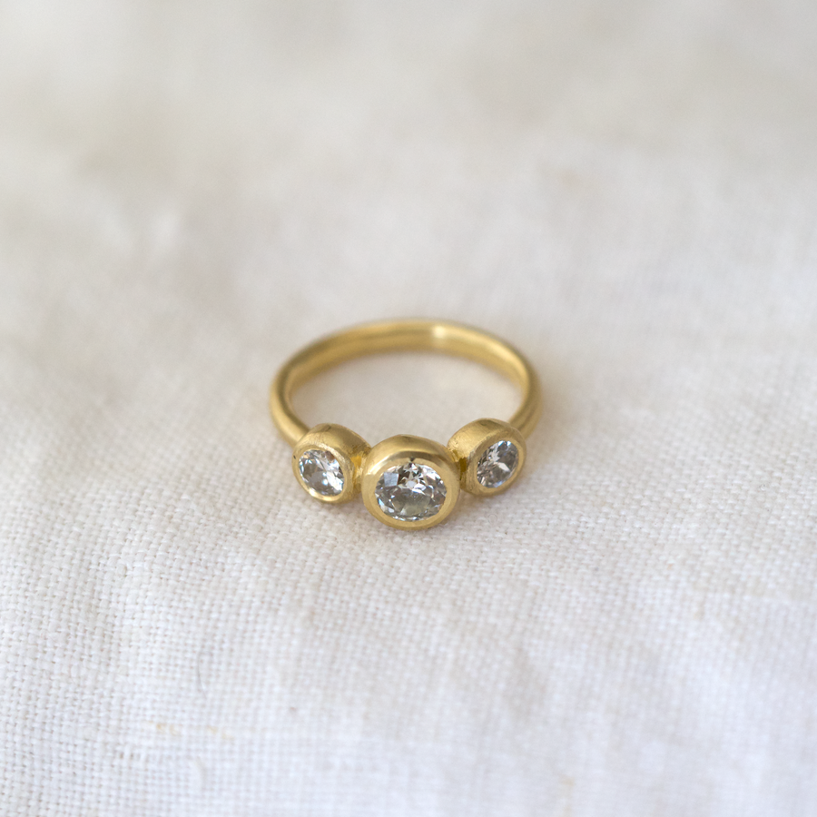 Gold ring with three clear gemstones on a white fabric background