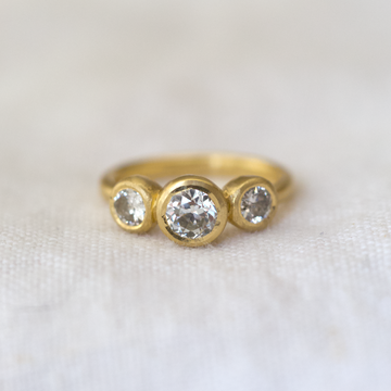 Gold ring with three vintage white diamonds on a white fabric background