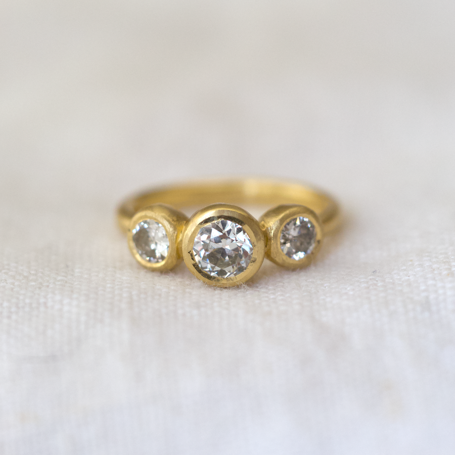 Gold ring with three vintage white diamonds on a white fabric background