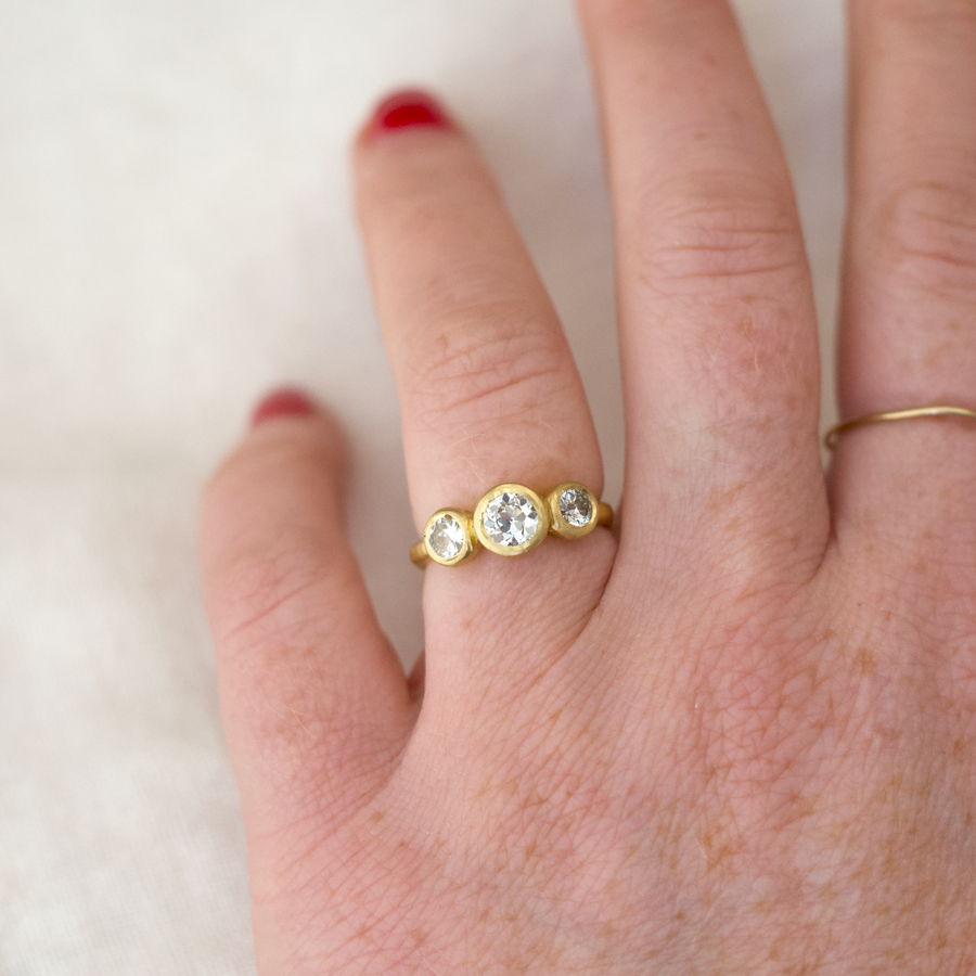 Gold ring with three clear stones on a hand against a white background