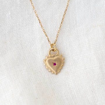 14k gold pendant in the shape of a hear with spiked edges, with a red ruby in the center, on 14k gold chain