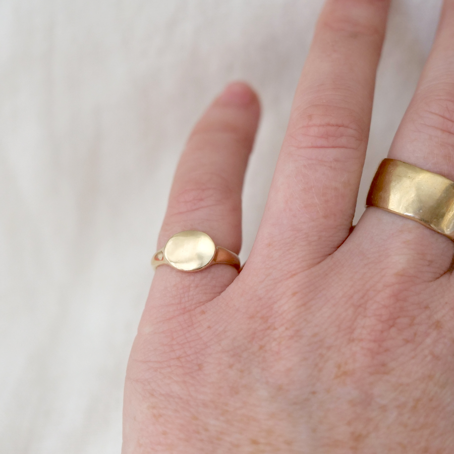 signet ring made of solid 14k gold with an oval face and high polish finish, on a models hand