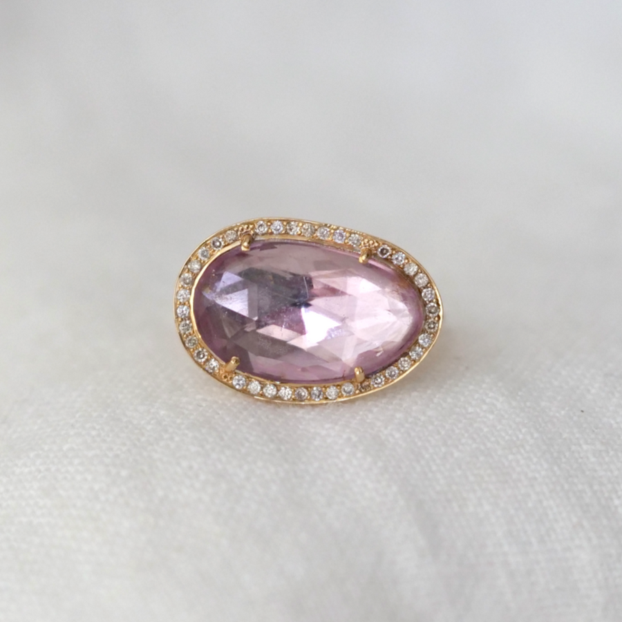 a large organically shaped pink tourmaline with white diamonds flush set all around it, set on a thin gold band 