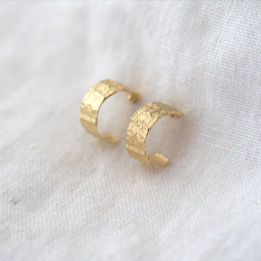 A subtle leaf texture is hand carved on the front of thin 14k gold hoops