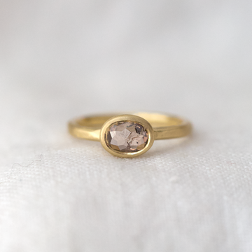 A beautiful one of a kind rose cut brown diamond, set in a simple oval bezel on a thin lightly textured square band