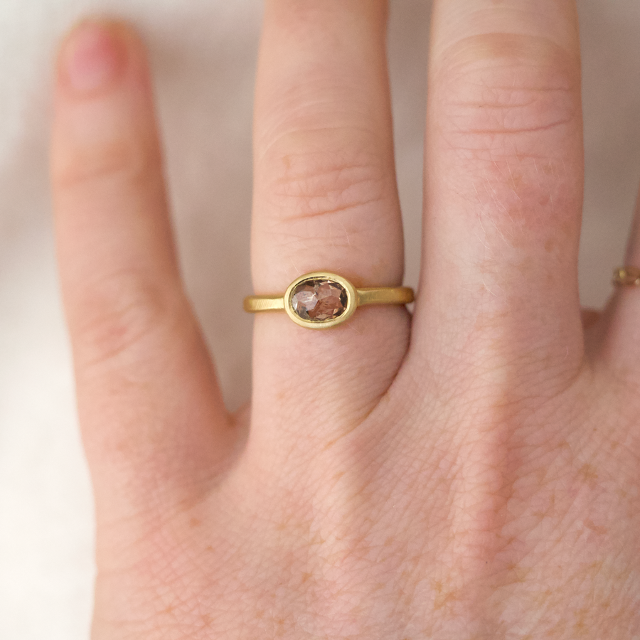 A beautiful one of a kind rose cut brown diamond, set in a simple oval bezel on a thin lightly textured square band, on models hand