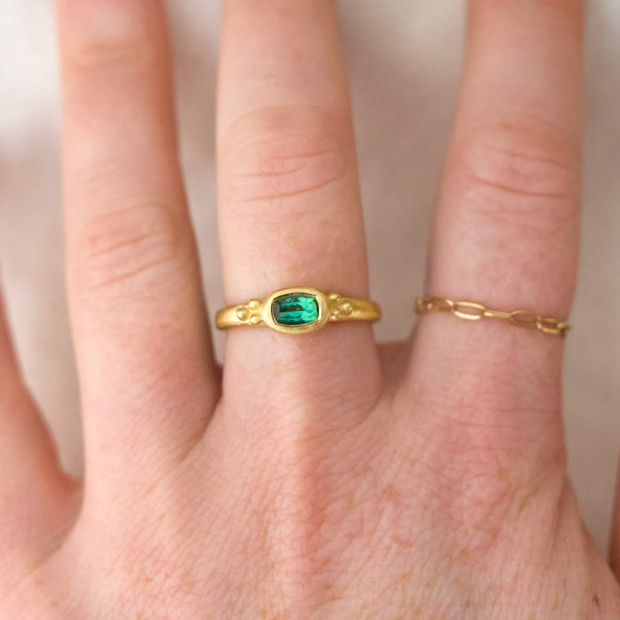 A brilliant rectangular tourmaline in a luxurious bezel setting, on a rounded band with three gold ball detailing on either side, on models hand