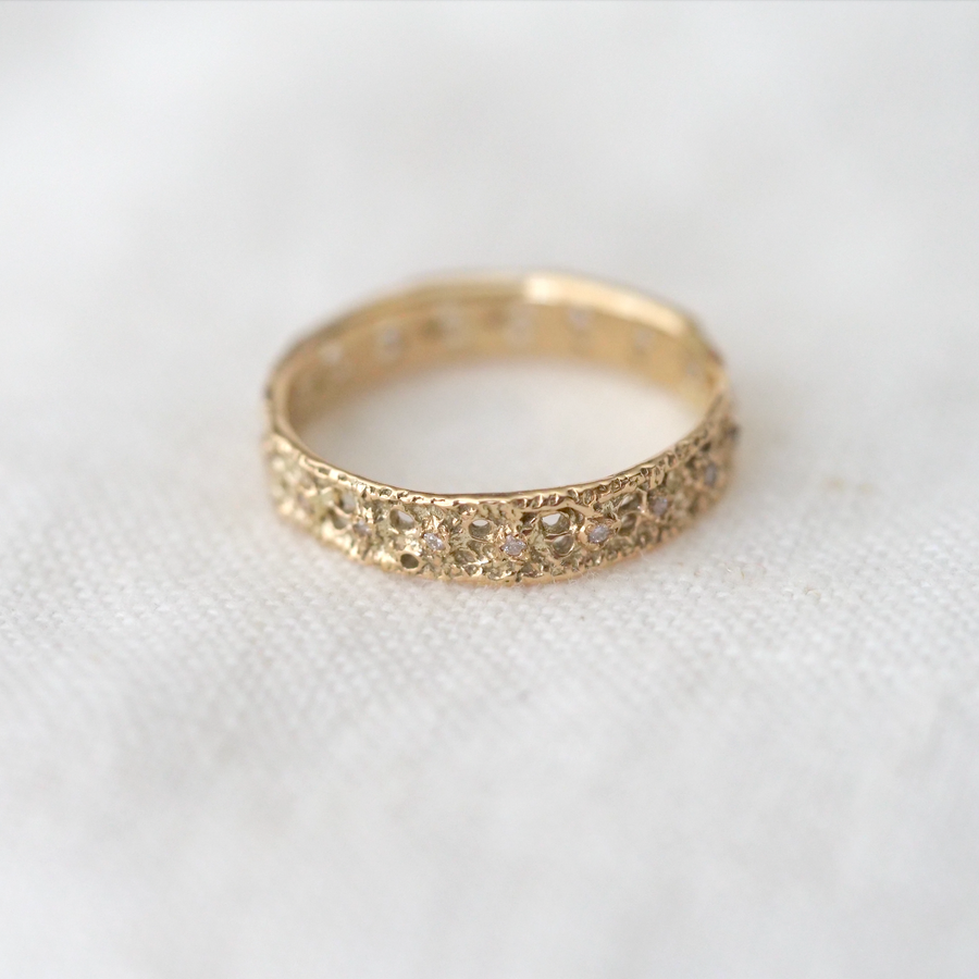 A ring with a lace motif. This is an eternity type ring with small diamonds all around, adding a subtle sparkle to a simple gold band.