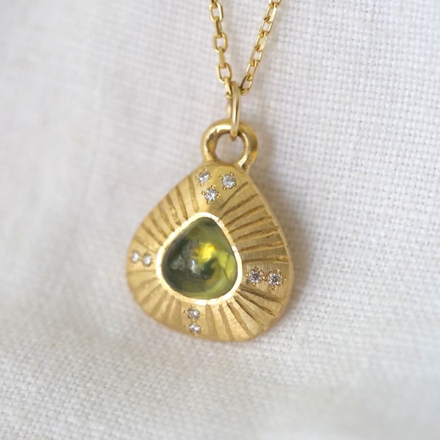 green sapphire cabochon set in 18K yellow gold and accented with ethically sourced diamonds, and engraved lines.