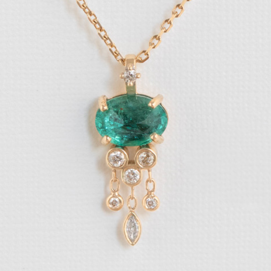 oval green emerald claw set in 14k gold with small white diamonds dangling from it, all hung on a gold 18k chain with a diamond encrusted bale 