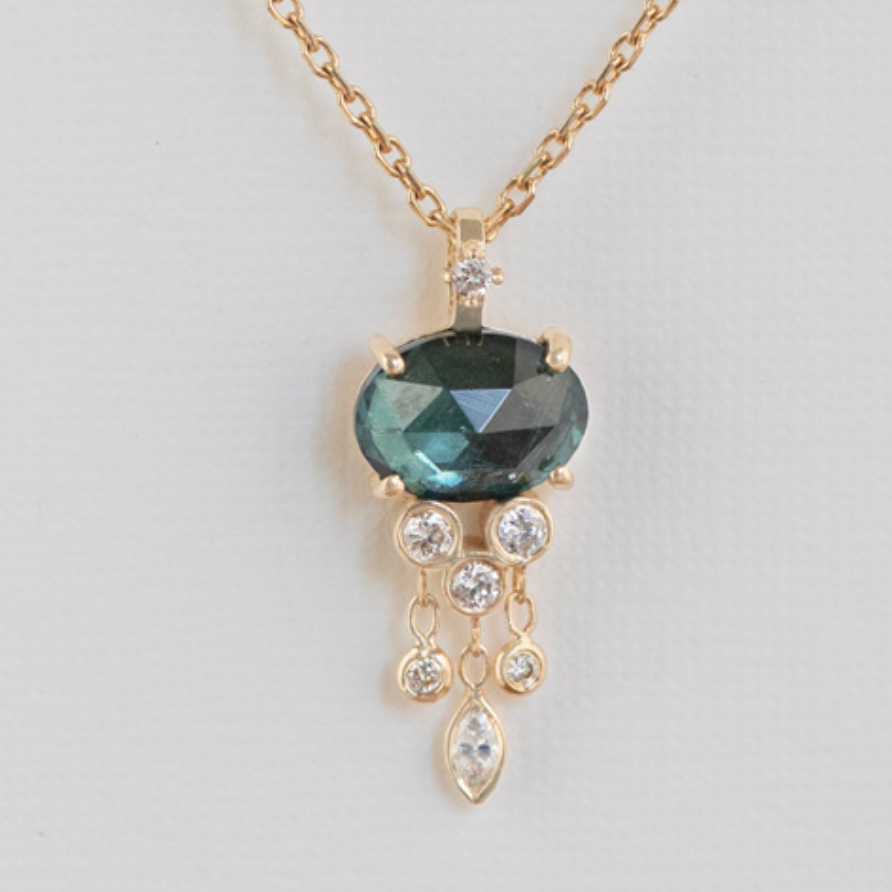 rose cut dark teal tourmaline claw set and hanging from a diamond set bail, with dangling white diamonds hanging form the bottom 