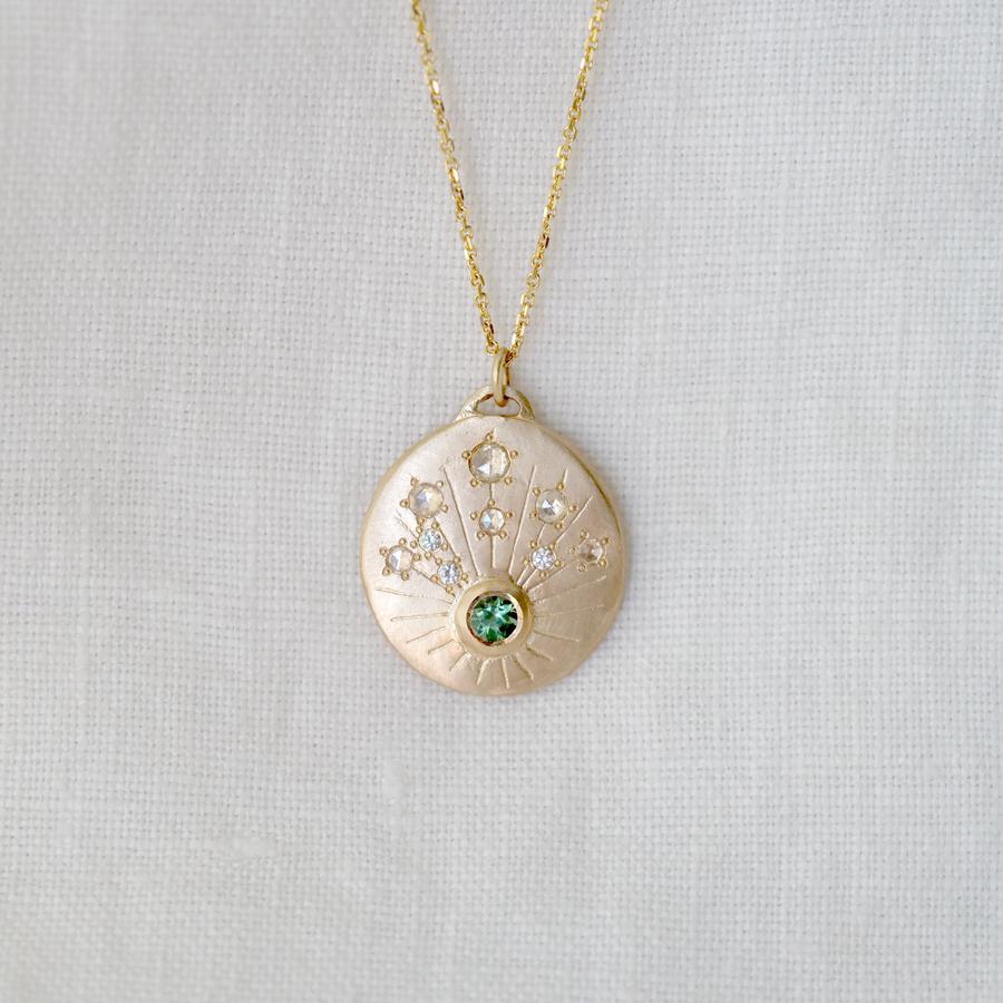 gold pendant has one bezel set tourmaline, with multiple rose cut champagne diamonds and three classic white diamonds creating the stars amongst the carved rays.