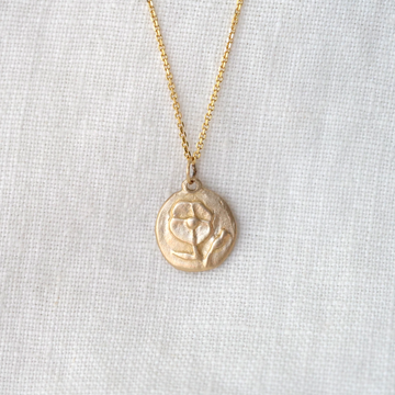 solid 14k gold round pendant with a poppy embossed on it, on a delicate 18 inch gold chain