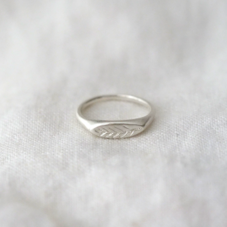 Silver band with hand engraved olive branch on face of signet laying on white linen
