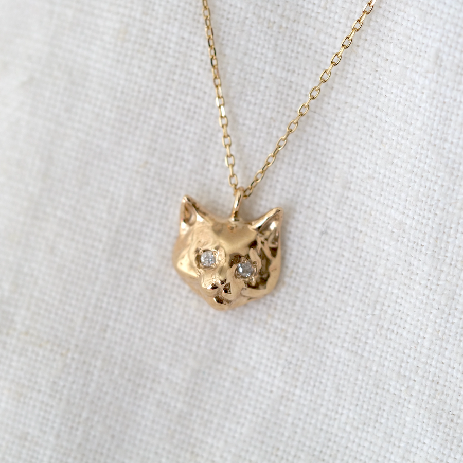 Solid gold 14k cat pendant set with two small white diamonds as the eyes