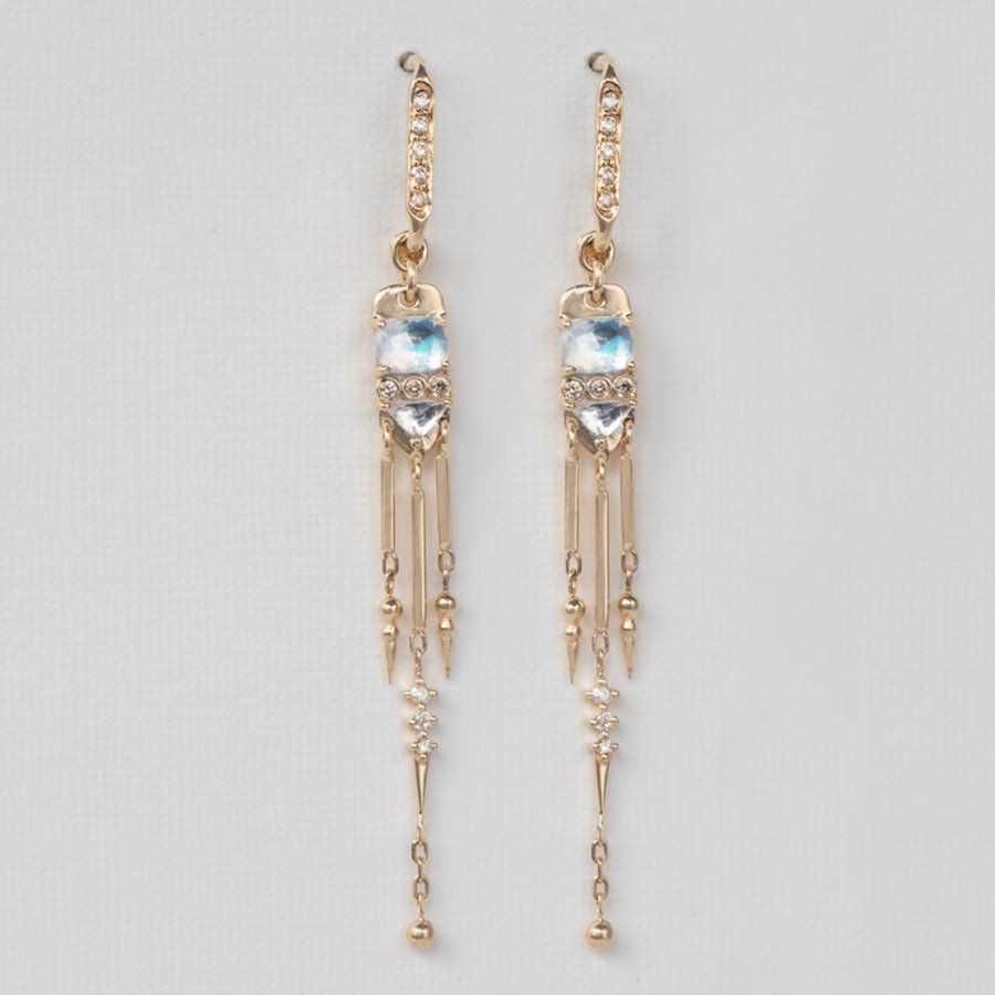 A pair of long dangling earrings featuring white diamonds set in gold, with iridescent moonstones and an articulated golden fringe hanging below.