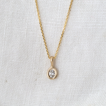 A diamond pendant necklace in 14k gold, displayed against a textured background.