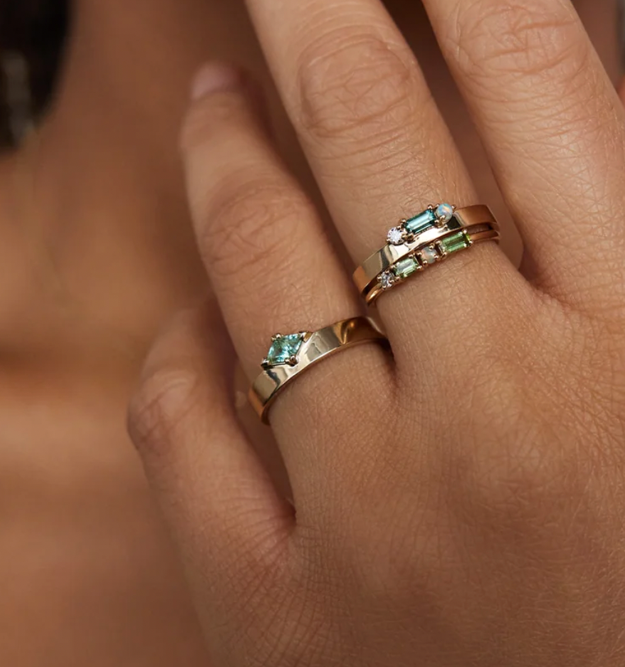 Close-up of a hand wearing two gold rings with green gemstones on a blurred background