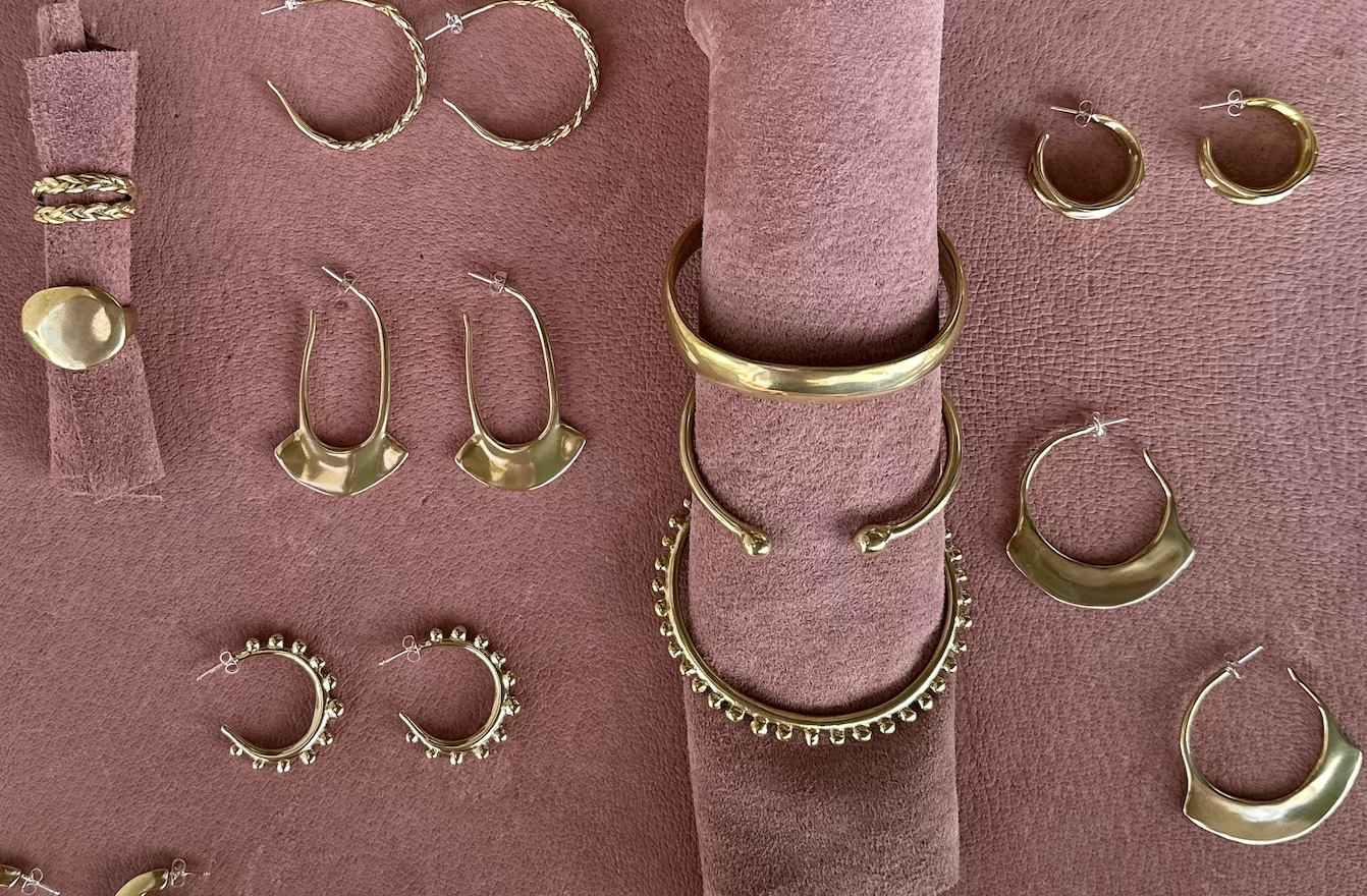 Brass earrings, bracelets and rings on pink suede backdrop 
