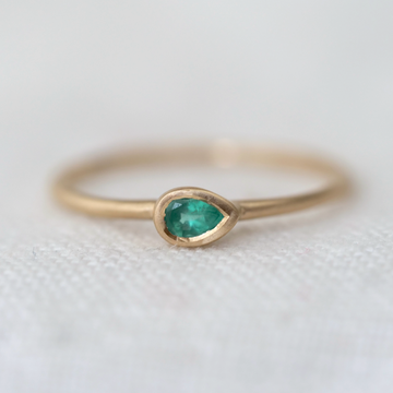 lightweight 14k gold band with a beautiful pear cut emerald bezel set in the center