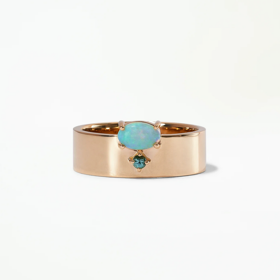 An oval opal sits atop a wide gold band while a small green tourmaline accents it underneath.