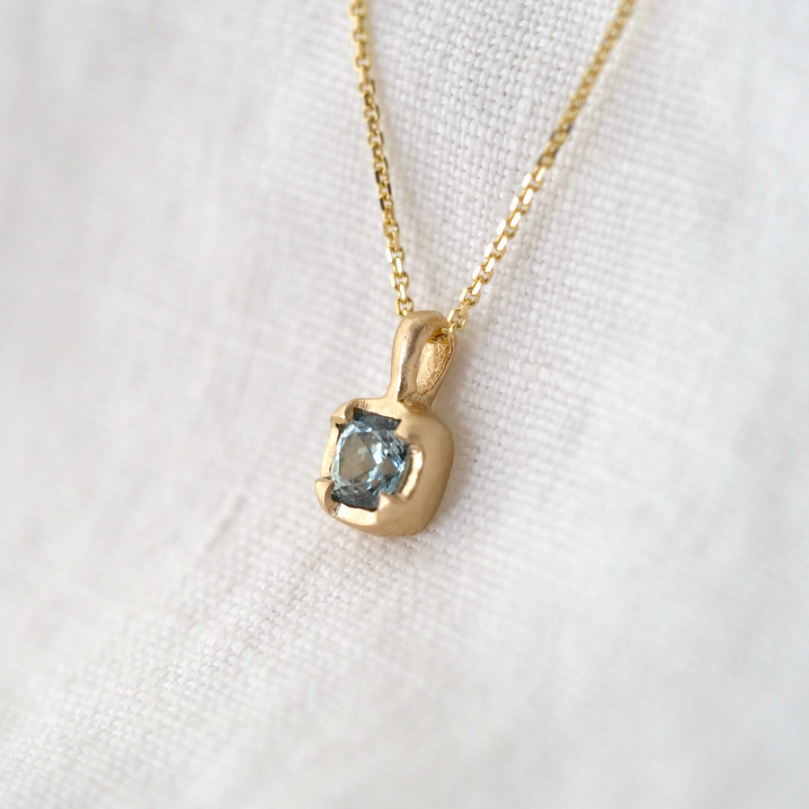 light blue montana sapphire set in gold on gold chain and white background