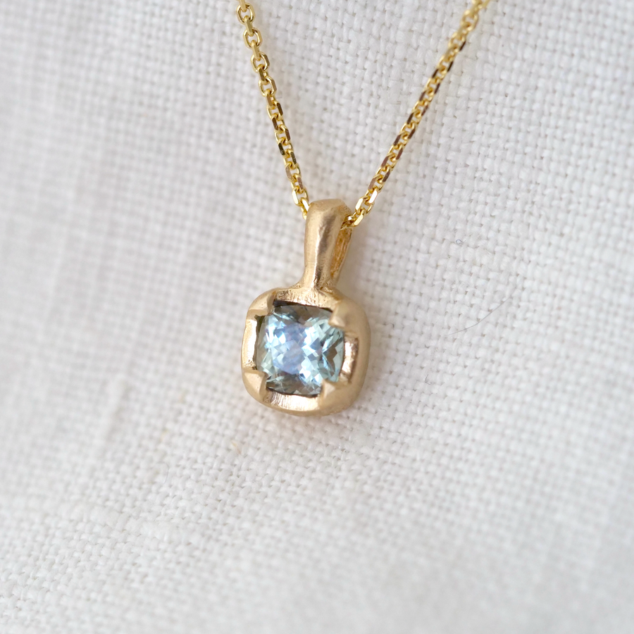 light blue montana sapphire set in gold on gold chain and white background