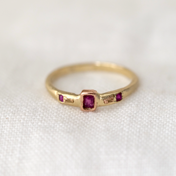 baguette ruby sits perfectly bezel set in 14k Rose Gold on a 14k Yellow Gold band, in between two gold rock sediment specs hand carved in 14k Rose Gold, and two flush set princess cut rubies