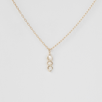 three stone diamond pendant on gold chain on white background
