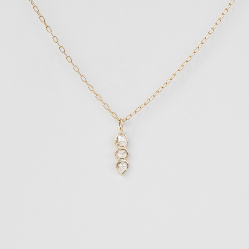 three stone diamond pendant on gold chain on white background