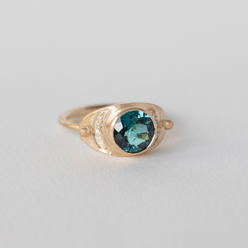 a radiant blue tourmaline is set between two diamond crescent moons, on a plate-faced style ring