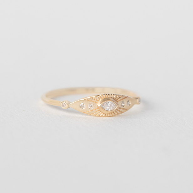 A white marquis diamond is surrounded by engraved rays in this 14k gold eye ring.