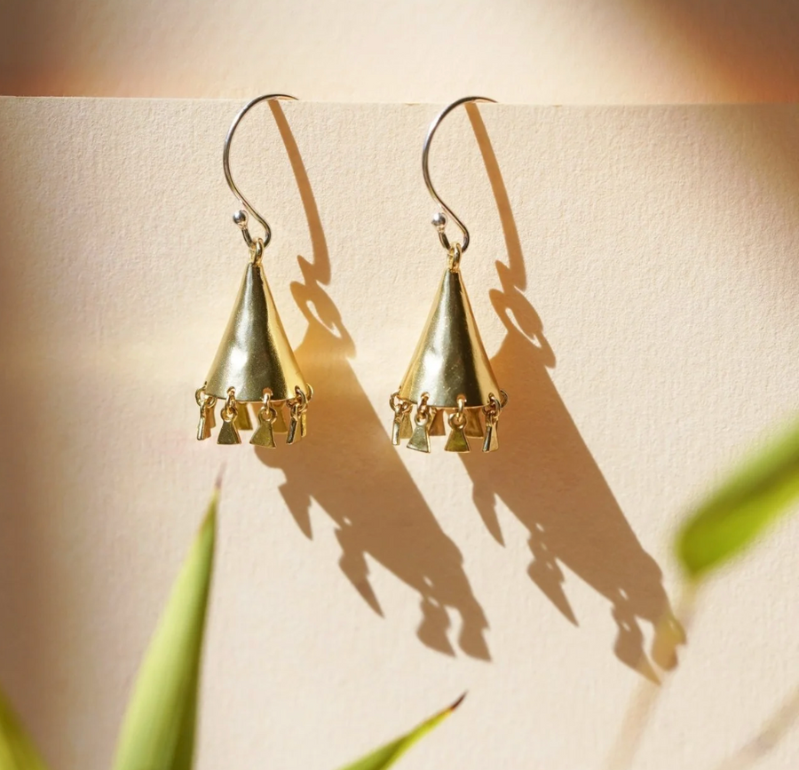 Gold triangle-shaped earrings on a beige background with plant shadows