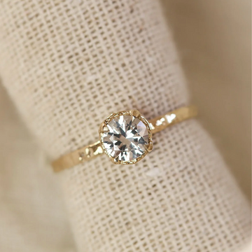 Gold ring with a diamond on a beige fabric background