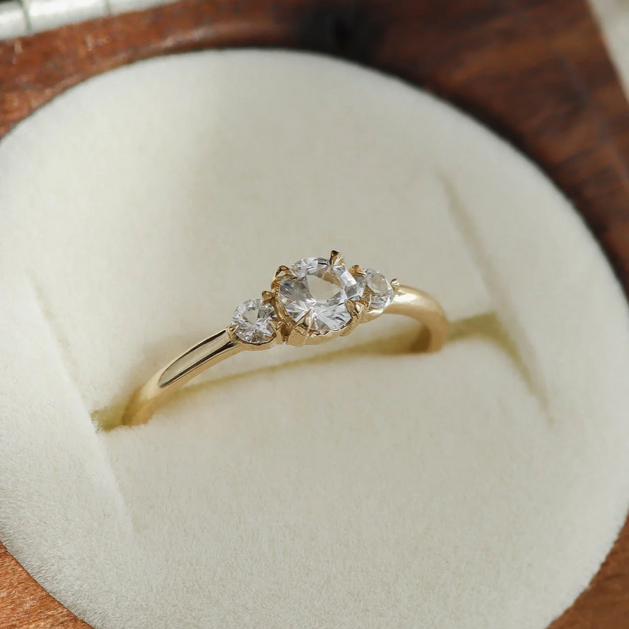 Gold ring with three diamonds on a white cushion