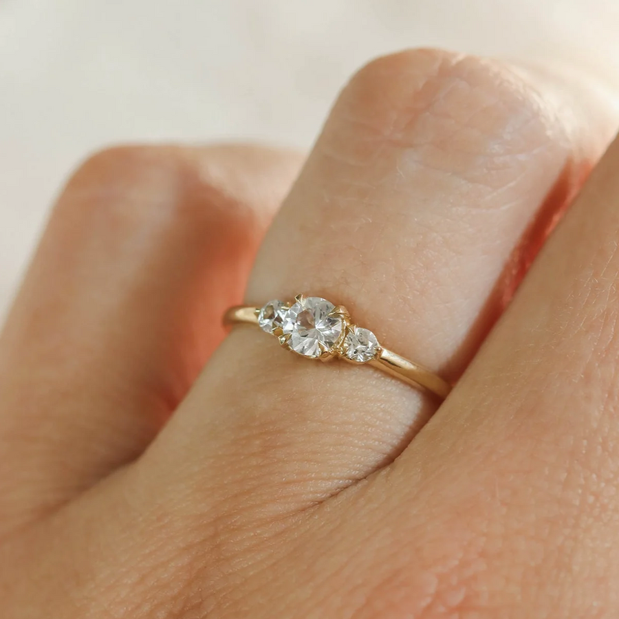 Gold ring with a diamond on a finger against a neutral background