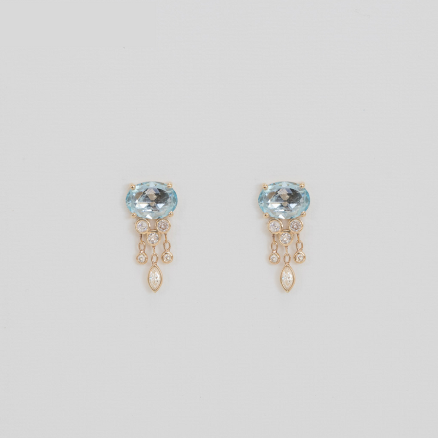 Pair of earrings with blue gemstones and gold and diamond accents on a light gray background