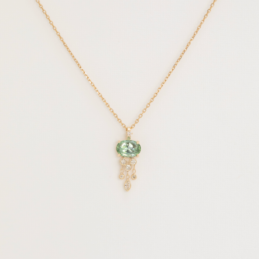 Gold necklace with a green gemstone pendant on a light gray background