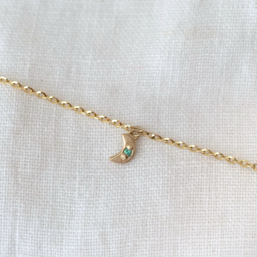 Gold necklace with a crescent moon pendant  with emerald green stone, on a white background