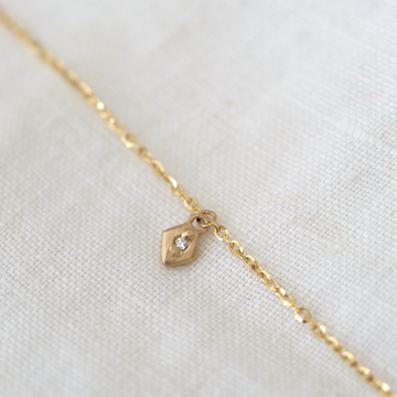 Gold necklace with a small pendant on a white fabric background