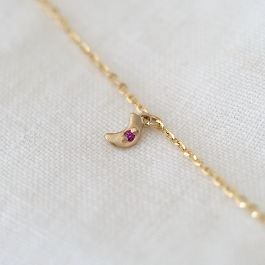 Gold necklace with a small moon pendant with pink sapphire on a white fabric background