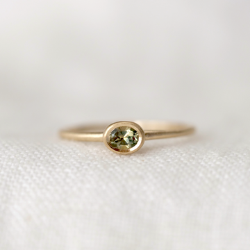 multicolor green and yellow sapphire set in bezel yellow 14k gold on a thin gold band, on a white background 
