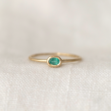 oval emerald set in 14k gold on a thin gold band, on a white back round 