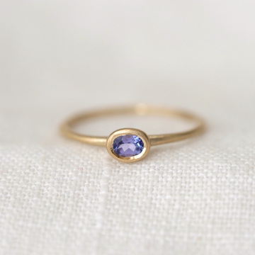 Gold ring with a purple tanzanite  gemstone on a white fabric background