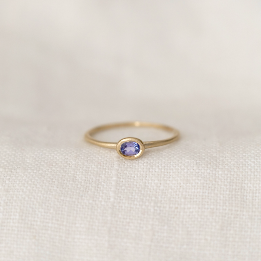 Gold ring with a purple gemstone on a light fabric background