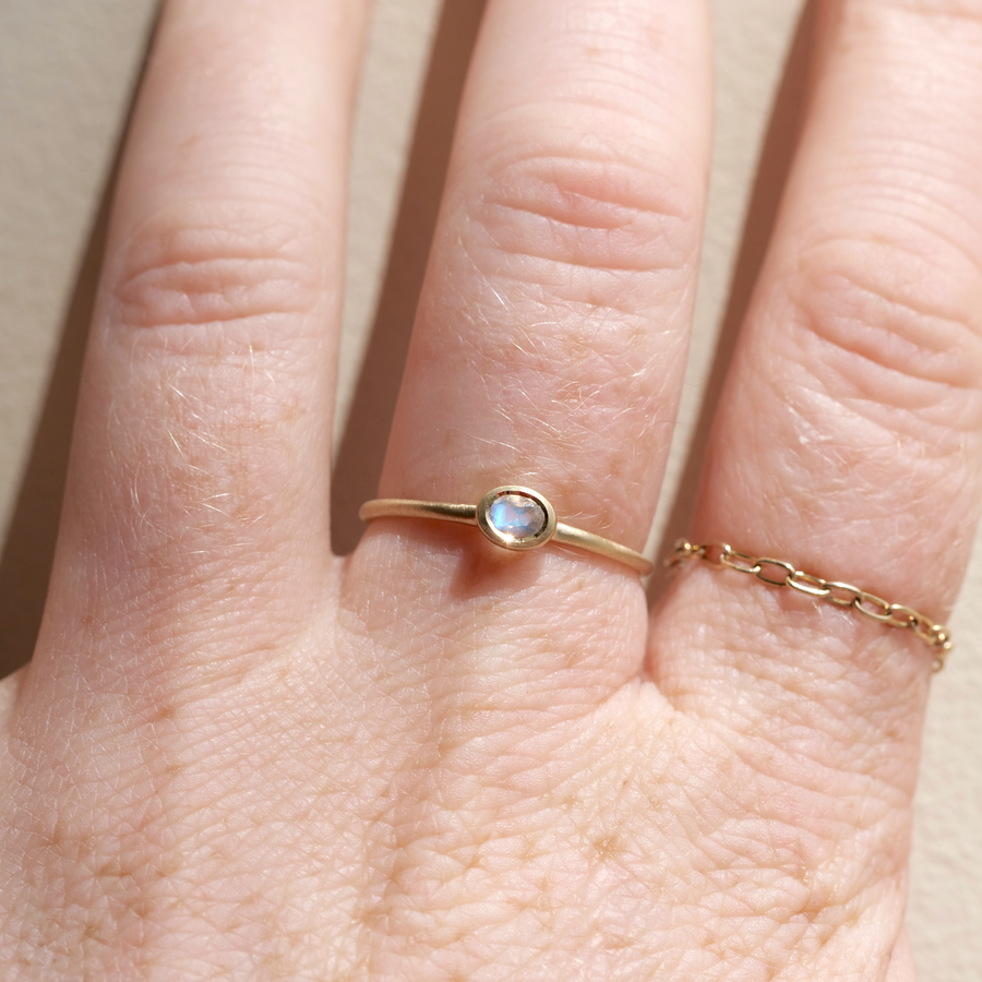 Gold ring with a small gemstone on a person's finger against a neutral background