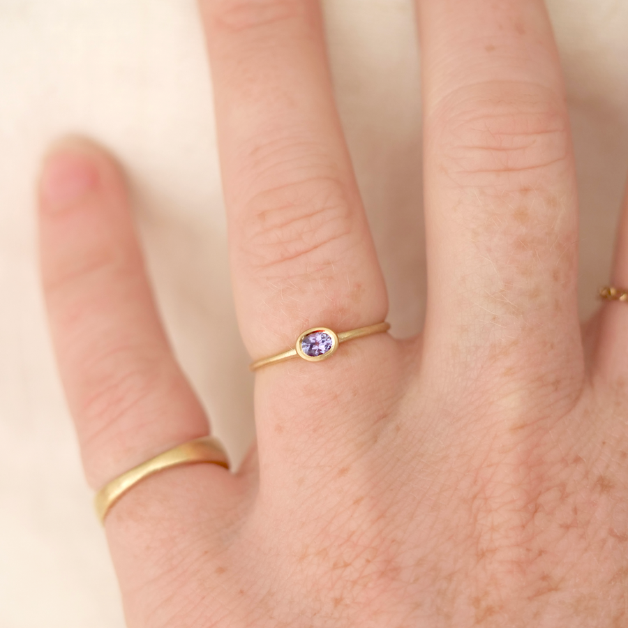 Gold ring with a purple gemstone on a person's finger against a neutral background