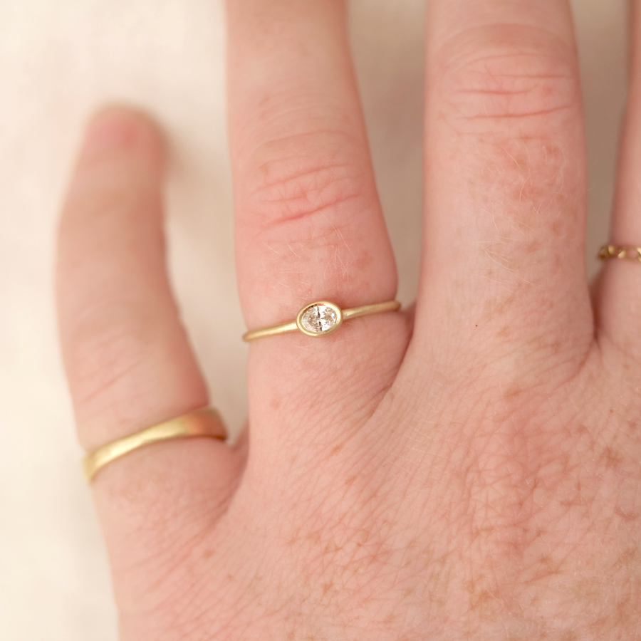Close-up of a hand wearing two gold rings with a small diamond on a light background