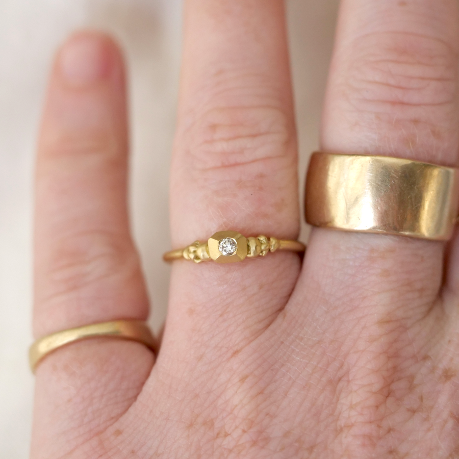 Close-up of a hand wearing three gold rings with a plain background