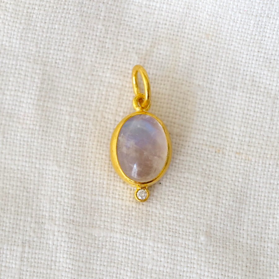 Gold pendant with a multicolored milky central stone and small diamond on a light fabric background